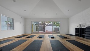Una habitación amplia con suelo de madera, colchonetas de yoga negras y un ventanal grande.
