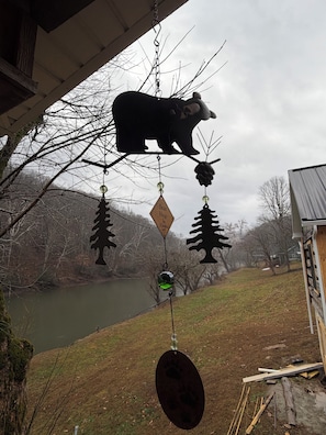 A wind chime with bear and tree silhouettes, a pond, and a house in the background.