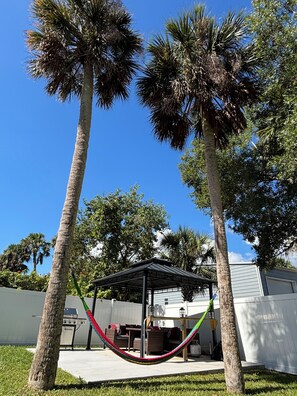 A backyard with two palm trees, a hammock, and a covered patio area. - Peaceful 3-bedroom house in Port Orange/South Daytona Beach (Port Orange)