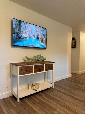 A room with a wooden console table, a television mounted on the wall, and a small statue on the wall. - Peaceful 3-bedroom house in Port Orange/South Daytona Beach (Port Orange)