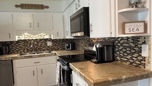Una cucina con mobili bianchi, un forno a microonde, una macchina da caffè e uno schienale piastrellato.