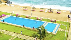 Un área de piscina con varias piscinas, una playa con tumbonas y sombrillas, y vistas al océano.