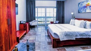 Habitación de hotel con una cama grande, un armario de madera, un escritorio con una silla y vistas al océano.
