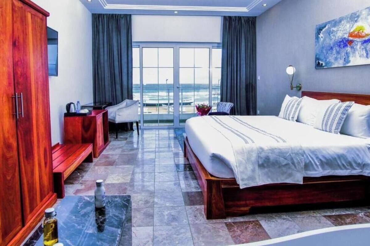 Habitación de hotel con una cama grande, un armario de madera, un escritorio con una silla y vistas al océano.