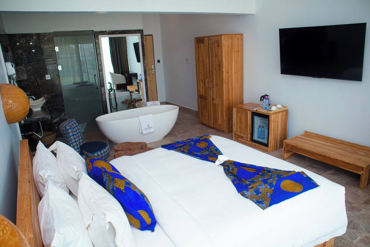 Una habitación de hotel con una cama grande, una bañera, un armario de madera, un televisor y un baño con cabina de ducha de vidrio.