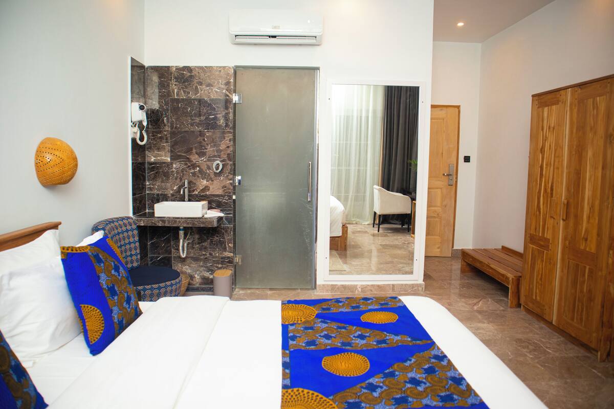 Habitación de hotel con cama, baño con pared de mármol, armario de madera y vista al pasillo.
