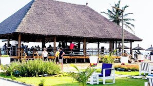 Una estructura junto a la playa con techo de paja, zonas de estar y vistas al océano.