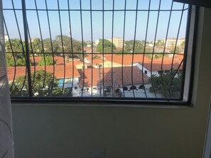 A window with metal bars, a view of buildings with red-tiled roofs, and greenery. - 1 bedroom apartment in Nyali Mombasa (Mombasa)