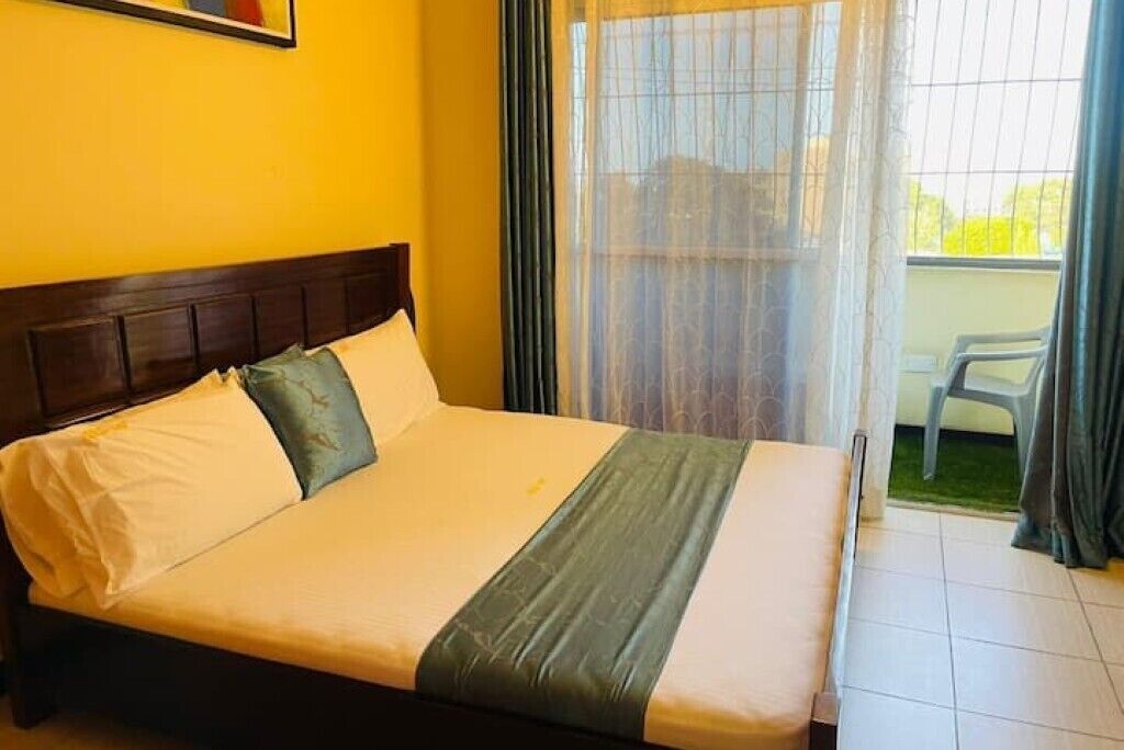 A single bed with a wooden headboard, a green blanket, and white bedding.