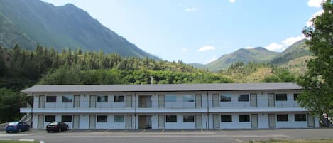 A motel with a simple, two-story structure, a parking lot, and a mountainous backdrop.