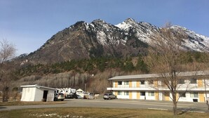 A motel with a parking lot, a small building, and a mountain in the background. - Retasket Lodge & RV Park (Lillooet)