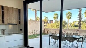 Eine moderne Küche mit einer großen Kochinsel, Gleitschiebetüren zu einer Terrasse mit Essplatz.