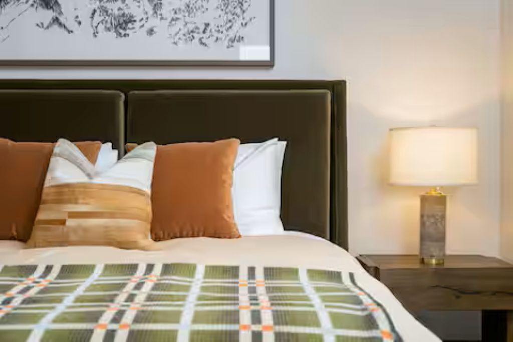 A neatly made bed with a patterned bedspread, a headboard, and a bedside lamp.