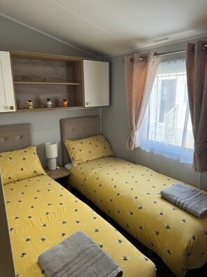 Een kamer met twee bedden, een plank met decoratieve objecten, een bedlamp en een raam met gordijnen.