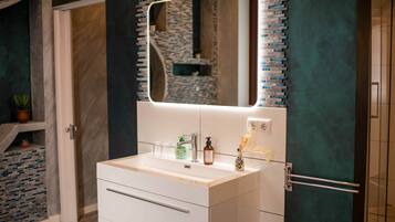 A bathroom with a white vanity, a mirror with a light, and a tiled backsplash.