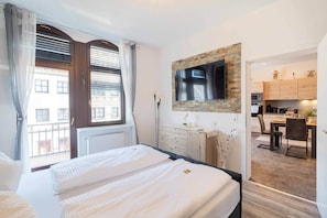 Ein Hotelzimmer mit Bett, einem an einer Ziegelwand montierten Fernseher, einem Schreibtisch und Blick ins Freie.