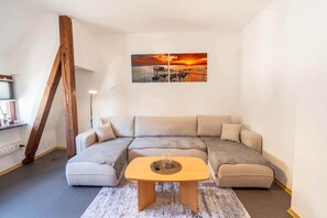 Ein modernes Wohnzimmer mit einer Eckcouch, einem Holztisch und einem Sonnenuntergangsbild an der Wand.