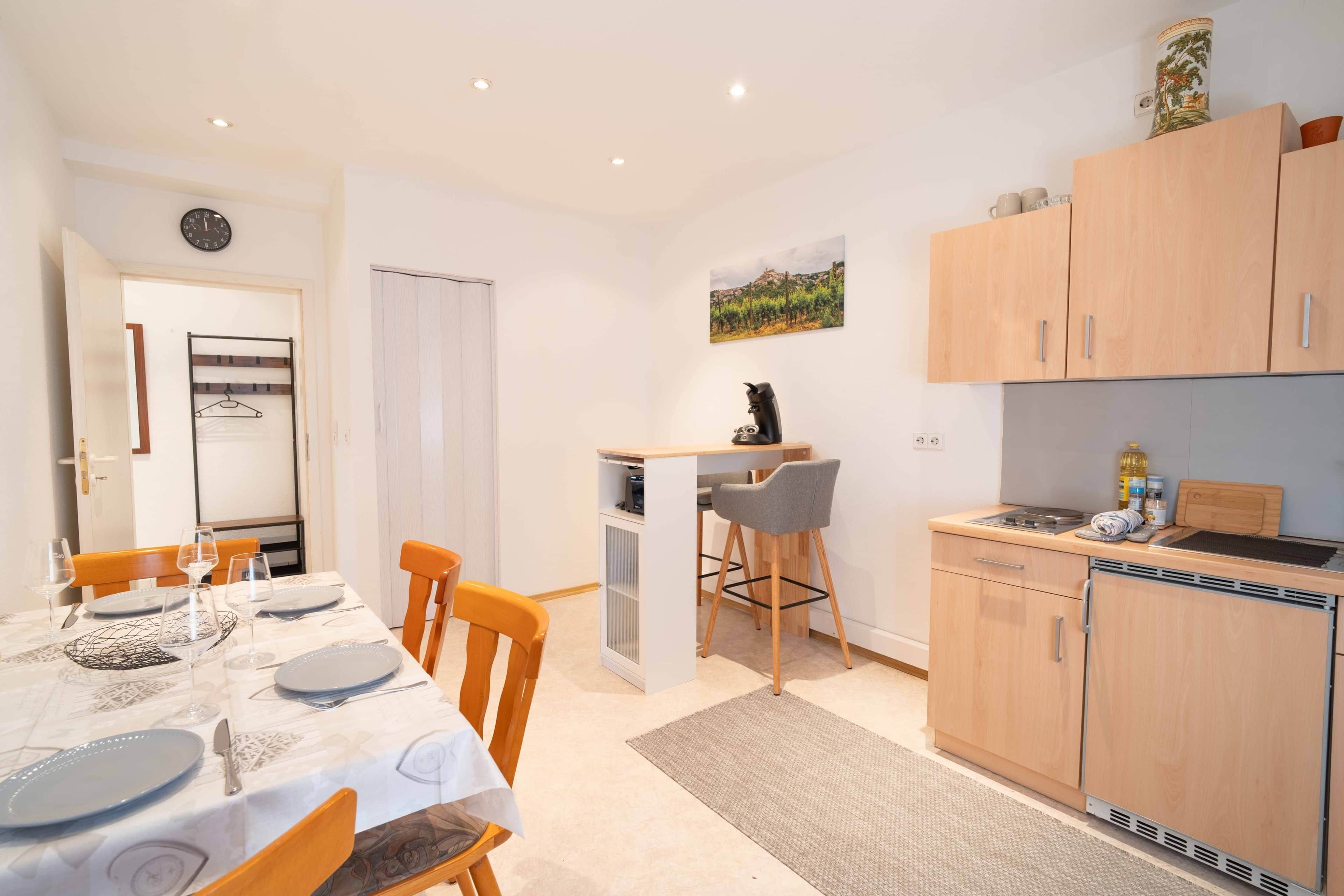 A compact kitchen with wooden cabinets, a dining area with a table set for two, and a small island with bar stools.