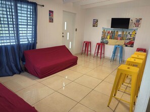 A room with a bed, a TV, a painting, and a set of stools. - Family-Friendly Townhouse | Pool & Outdoor Dining (Cobo Rojo)
