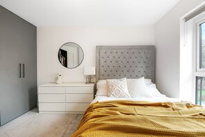 A bedroom with a bed, a dresser, a mirror, and a window. - Luxurious 2 bed Flat in Greenhithe (Greenhithe)