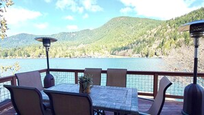 A wooden deck with a table and chairs, overlooking a lake and forested hills. - Amazing Lakefront home on Lake Sutherland, WA (Port Angeles)