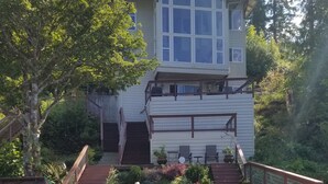 A wooden deck with a dog and a person, a house with a balcony, and a small water feature. - Amazing Lakefront home on Lake Sutherland, WA (Port Angeles)