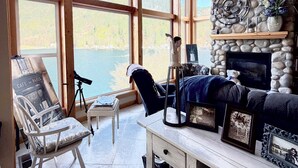 A room with a stone fireplace, large windows, a telescope, and a cozy seating area. - Amazing Lakefront home on Lake Sutherland, WA (Port Angeles)