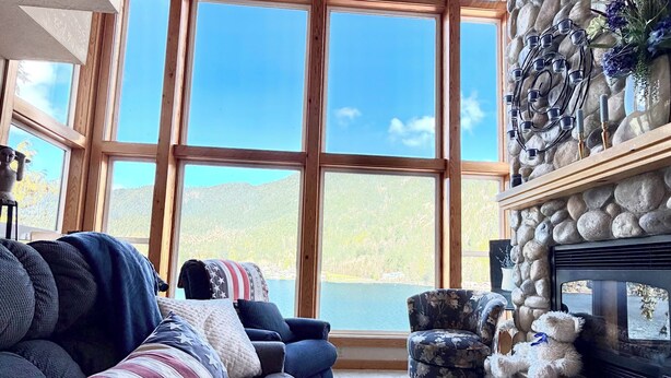 A living room with a stone fireplace, large windows, a sofa, and a patterned rug. - Amazing Lakefront home on Lake Sutherland, WA (Port Angeles)