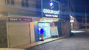A street scene with a building featuring a neon sign for 'Cooler City' and a closed shop with a sign for 'Sky Tel.' - A clean studio Apartment in Nyali, Mombasa. (Mombasa)