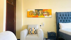 A hotel room with a bed, a chair, a small table, a wall-mounted painting, and a wardrobe. - A clean studio Apartment in Nyali, Mombasa. (Mombasa)