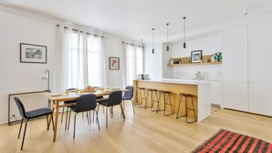 A modern kitchen with a dining area, wooden flooring, and a bar stool setup. - Stylish 2BR in Private Mansion at Rue de Passy (Paris)