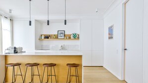 A modern kitchen with white cabinets, a wooden countertop, and three stools. - Stylish 2BR in Private Mansion at Rue de Passy (Paris)