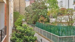 A narrow urban street with a brick building, a green fence, and lush greenery. - Stylish 2BR in Private Mansion at Rue de Passy (Paris)