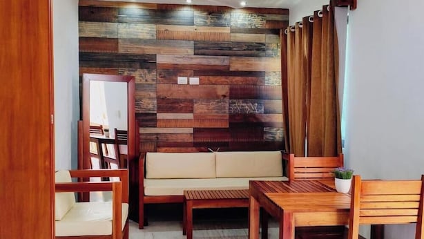 A room with a wooden wall panel, a sofa, a dining table, and chairs. - Departamentos Túumben Ché (Valladolid)