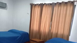 A room with two beds, a wooden nightstand, and a window with curtains. - Departamentos Túumben Ché (Valladolid)
