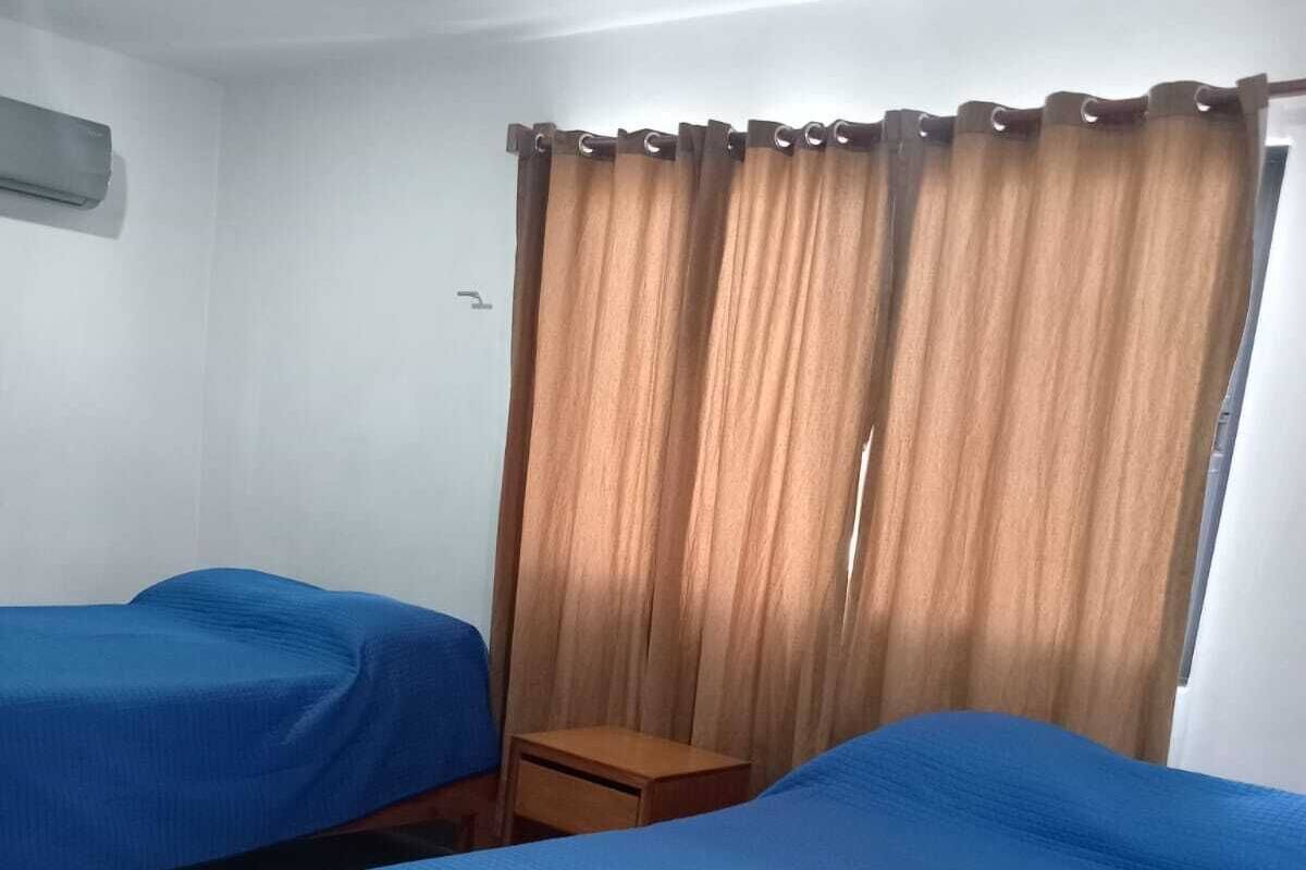 A room with two beds, a wooden nightstand, and a window with curtains.
