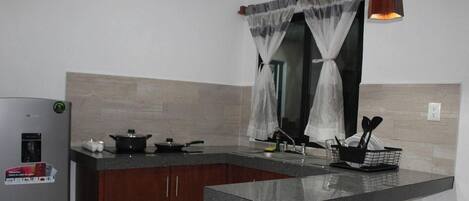 A kitchen with a refrigerator, stove, and utensils.
