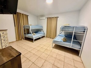 A room with two bunk beds, a dresser, an air conditioning unit, and a television. - Beachside Townhouse: Pool and BBQ for Groups (Cabo Rojo)