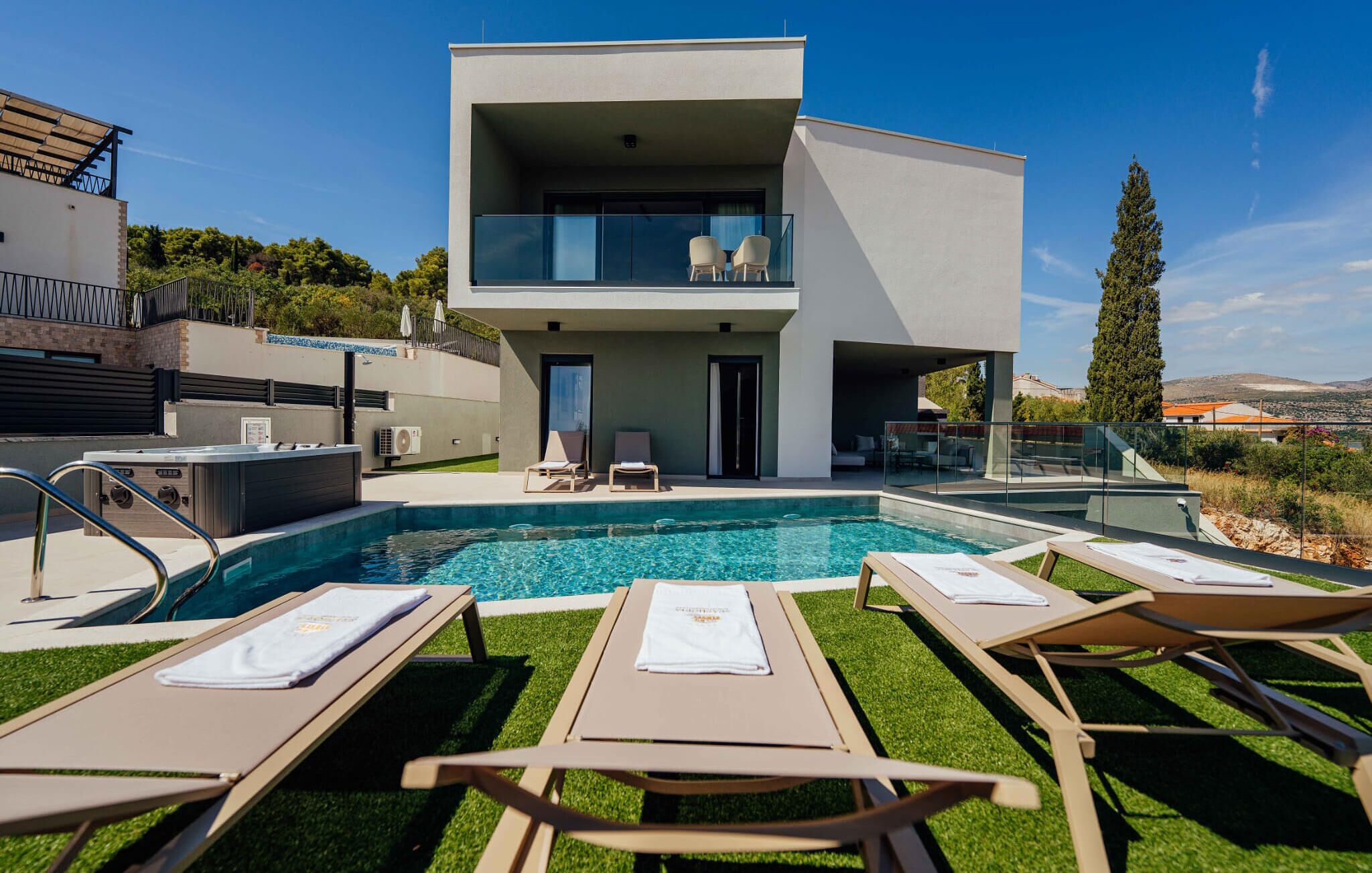 A modern two-story building with a swimming pool, lounge chairs, and a glass balustrade.
