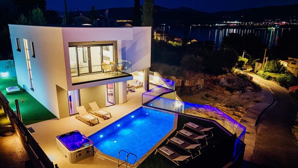 Et moderne hus med swimmingpool, udendørs møbler og et spabad.