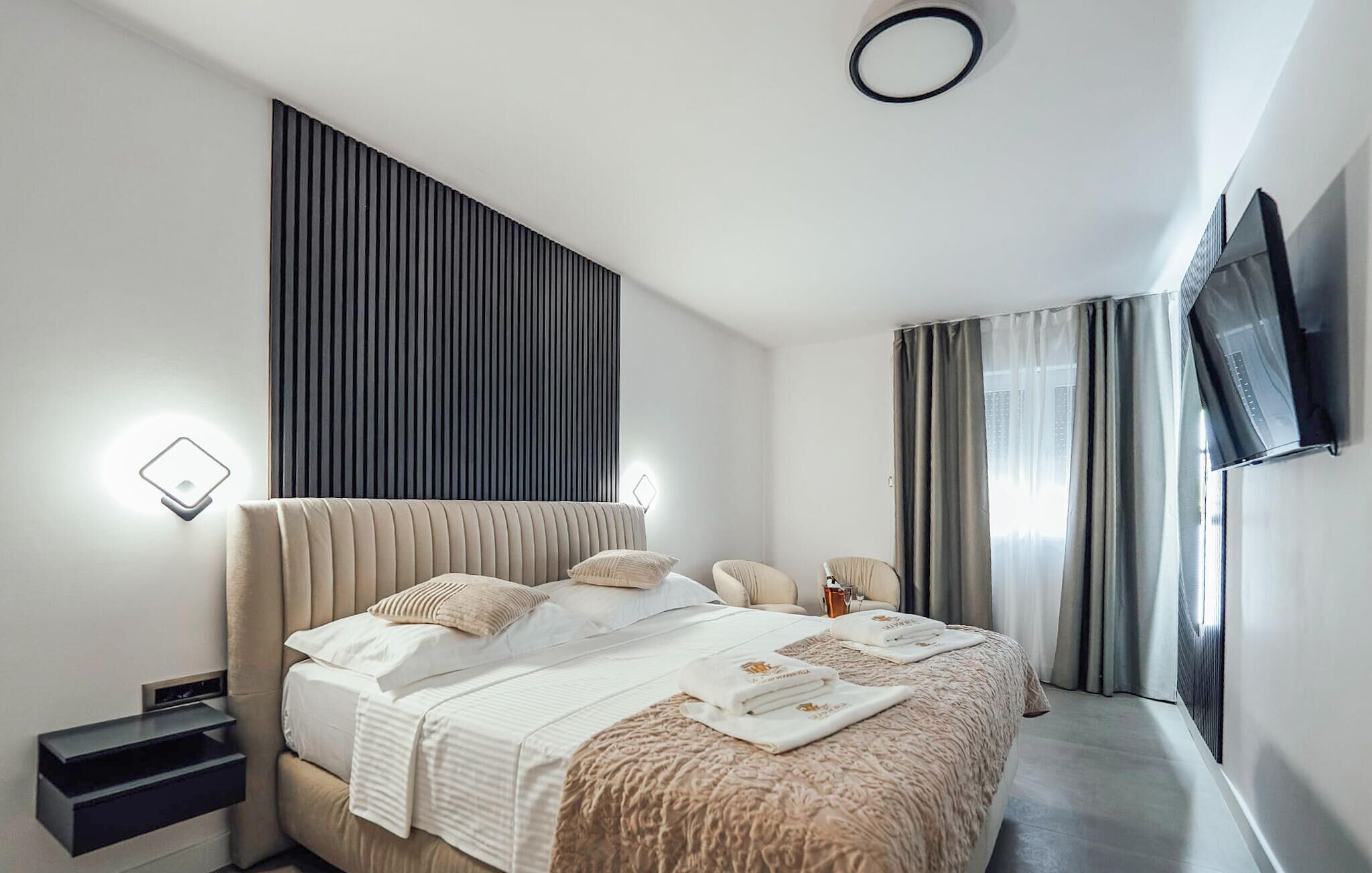 A modern hotel room with a large bed, bedside tables, a flat-screen TV, and a window with curtains.