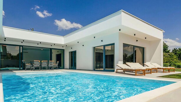 Une maison moderne dotée d’une piscine, de grandes portes vitrées et d’un espace salon extérieur.