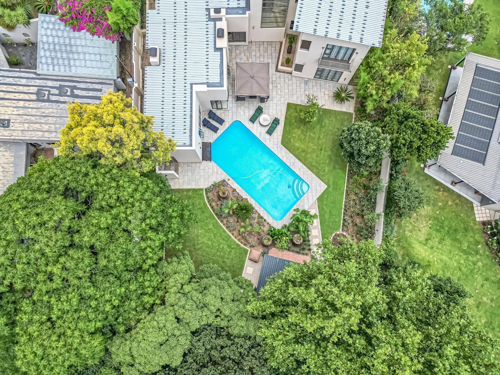 An aerial view of a residential area with a swimming pool, green lawns, and modern houses.