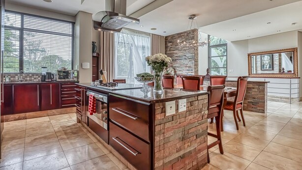 Une cuisine moderne dotée d’un îlot central, d’un coin repas avec des chaises rouges et d’une grande fenêtre qui laisse entrer la lumière naturelle.