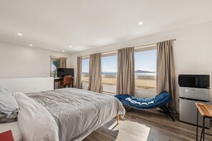 A bedroom with a bed, a desk, a chair, a sofa, a TV, a microwave, and a view of the desert. - Bay Breeze Retreat | Water Front, Family Friendly (Richmond)