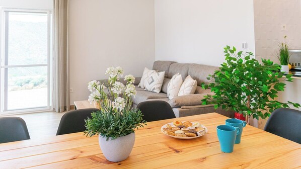 Un coin repas avec une table en bois, une assiette de pâtisseries, une plante en pot et une tasse bleue.