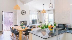 Eine moderne Küche mit Kochinsel, einem Essbereich mit Holztisch, schwarzen Stühlen und Pendelleuchten.