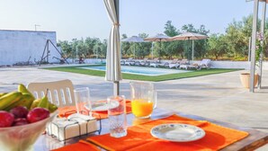 Ein Essbereich im Freien mit einem für das Frühstück gedeckten Tisch, einem Pool im Hintergrund und Liegestühlen.