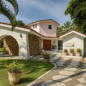 A two-story house with a stone archway, a central door, and a small attached structure with potted plants.