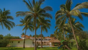 A resort with a pool, palm trees, and a thatched-roof structure.